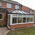 A brick and glass conservatory with a sloping roof and uPVC frames is attached to the back of a house in West Sussex.