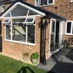 A sunlit brick conservatory with large uPVC windows and a glass roof stands attached to a house in West Sussex.
