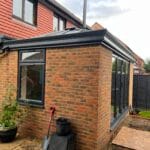 Single-storey brick house extension in West Sussex with large uPVC windows and glass doors, black roof trim, and a small garden area.