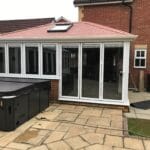 A brick house in West Sussex with a modern conservatory featuring large uPVC glass doors and windows with a skylight on the red-tiled roof.