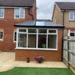 A brick conservatory with large uPVC windows and a black tiled roof is attached to the back of a house in West Sussex.