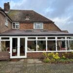A brick house in West Sussex with a large uPVC glass conservatory at the back, featuring multiple windows and doors.