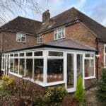 A brick house with a pitched roof and white-framed uPVC glass conservatory on a cloudy day in West Sussex.