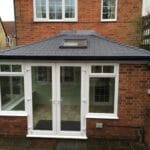 A modern brick house extension in West Sussex with white uPVC-framed glass doors and windows, a dark tiled pitched roof, and a skylight, seen from the outside on a stone patio.