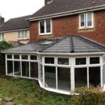 A modern brick house in West Sussex with a dark tiled roof features a large uPVC white-framed conservatory extension with many windows.