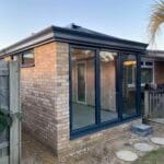 A modern brick extension in West Sussex with large uPVC glass sliding doors and a small window, featuring a flat roof.