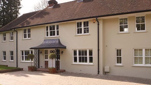 A large beige two-storey house in Horsham with white uPVC-framed windows, a black door canopy, brick steps, and two potted topiary plants at the entrance.