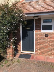 A dark grey composite front door with a letterbox is set in a red brick house. White jasmine flowers climb the wall to the left of the door.