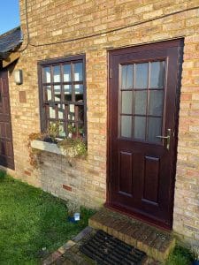 A brown composite door with a glass panel is set in a brick wall next to a matching uPVC window.