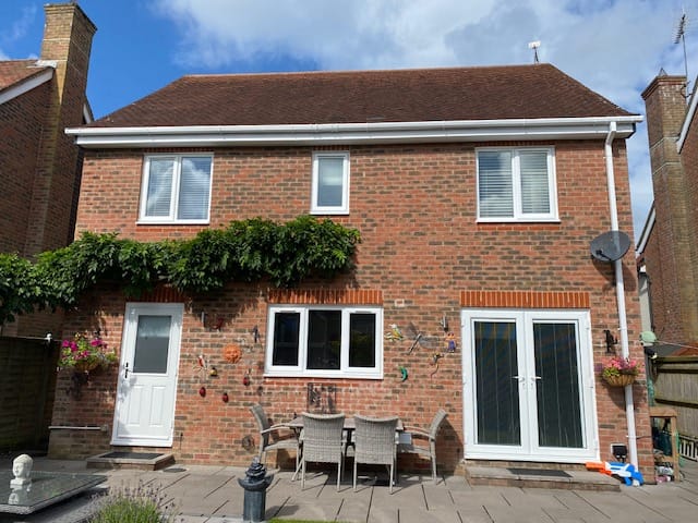 White uPVC replacement windows installed by Window Mart in Horsham, a white composite door, and glass patio doors. Garden furniture, potted plants, and wall-mounted decorations sit in the paved back garden.