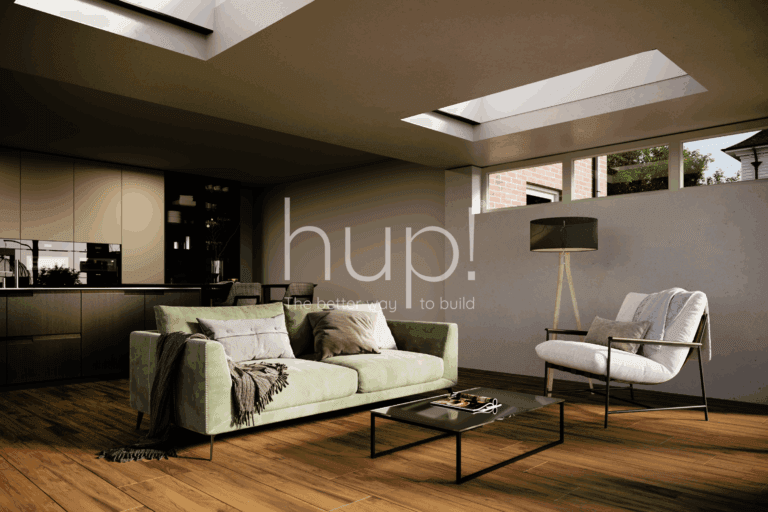A modern Horsham Hup! extension with a green sofa, armchair, standard lamp, and coffee table on wooden flooring; skylights in the ceiling and kitchen cupboards are visible in the background.