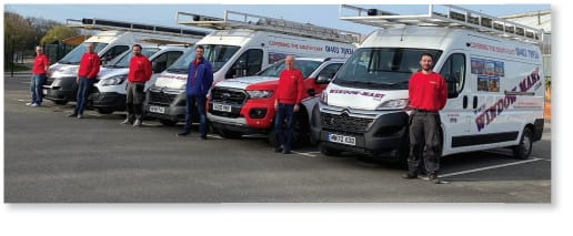 Five Window-Mart uPVC installers in uniforms stand beside four white company vans branded for uPVC services in Horsham and one red vehicle, all parked in a row. The vans display company branding and have ladders mounted on their roofs.