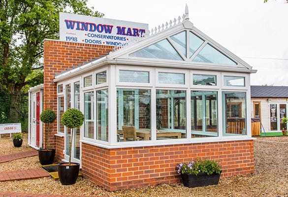 A glass conservatory with a brick base stands outside Window Mart in Horsham, offering uPVC doors and windows.