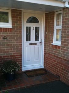 A white composite front door with a silver handle and letterbox, set in a red brick exterior in West Sussex. There’s a semicircular window above, a doormat in front and a potted plant to the left.