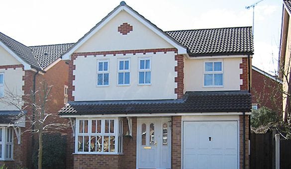 A two-storey detached house in Horsham with a tiled roof, uPVC white-framed windows, and an integral garage. The exterior features brickwork around the windows and corners, plus a small front garden with a tree.